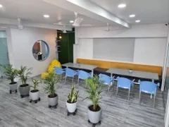 Cafeteria and breakout area at Adroit Infosol with seating, a projector screen, and potted plants